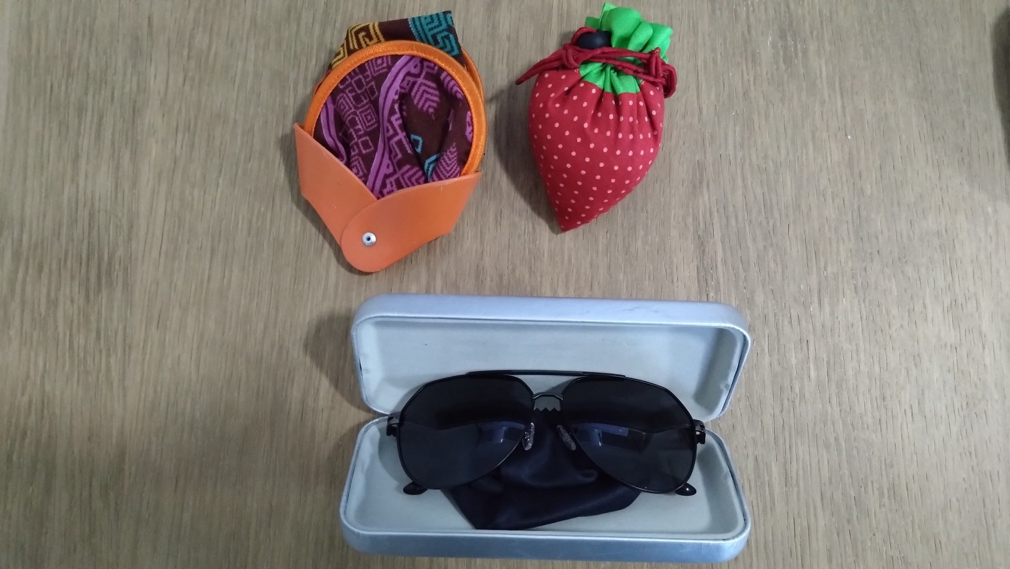 A folding fan, sunglasses in a glasses case, and a reusable shopping bag shaped like a strawberry.